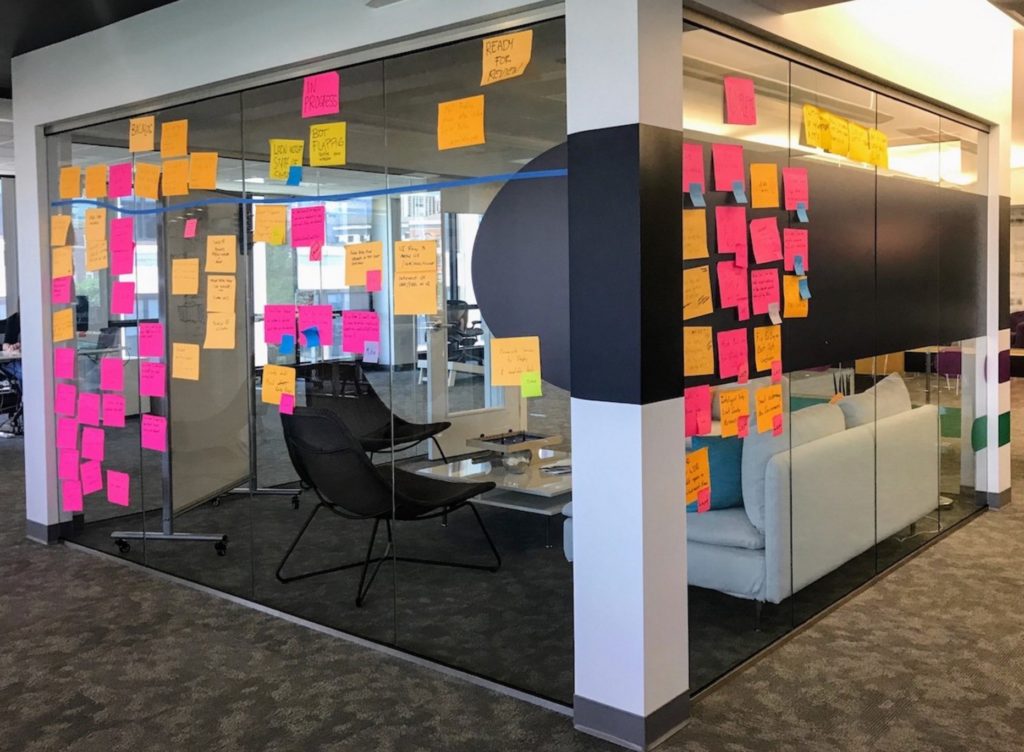 An office with glass walls and tons of colorful post it notes all over the outside.